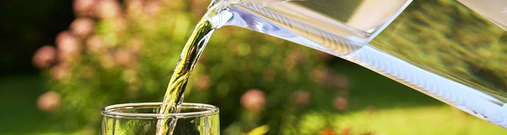 Water being poured into a glass from a glass pitcher, outdoors