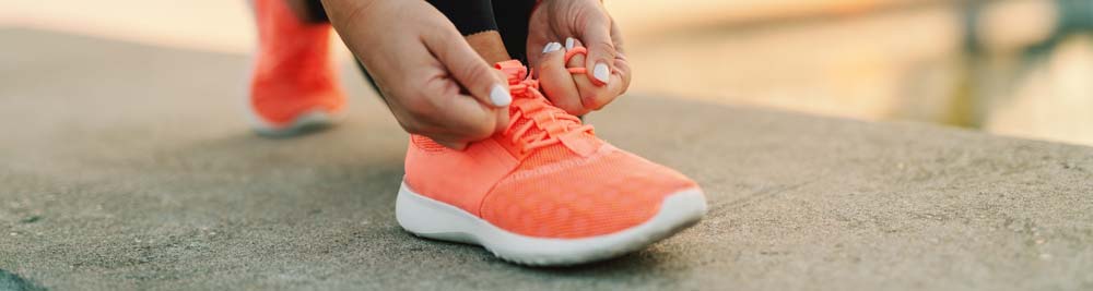 A woman tying the laces to her running shoes while standing on a concrete ledge