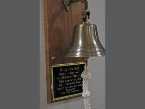 A bell with a plaque that reads, "Ring this bell three times well to celebrate this day. This course is run, my treatment is done, now I am on my way. Donated by Kat & Roy Burkhalter"