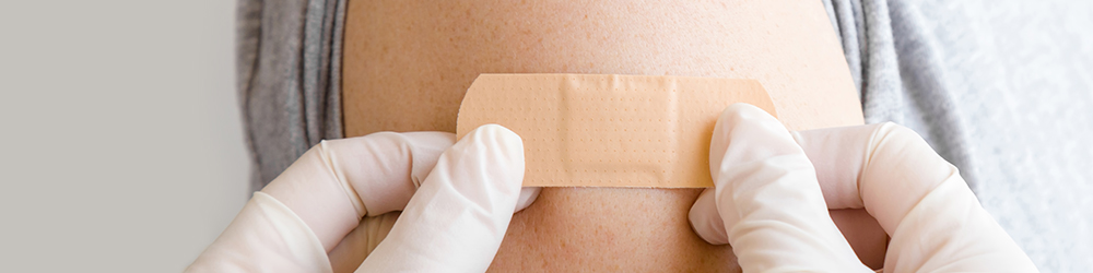 A nurse wearing gloves putting a bandaid on the arm of someone