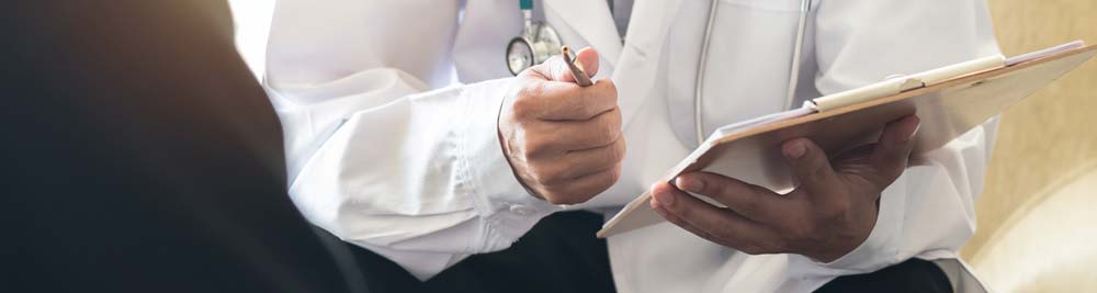 A doctor holding a pen and clipboard talking to a patient