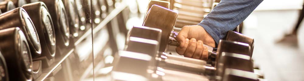A man picking up a freeweight from a large rack of freeweights
