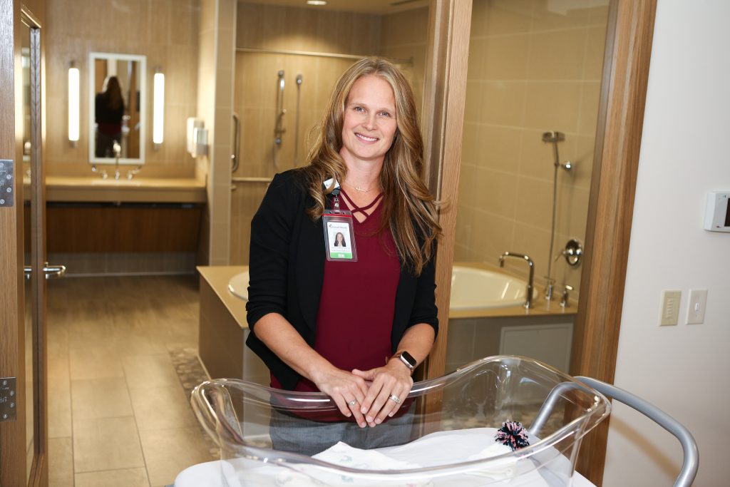 Carrie Lord standing in front of a birthing tub with her hands resting on a clear plastic bassinet
