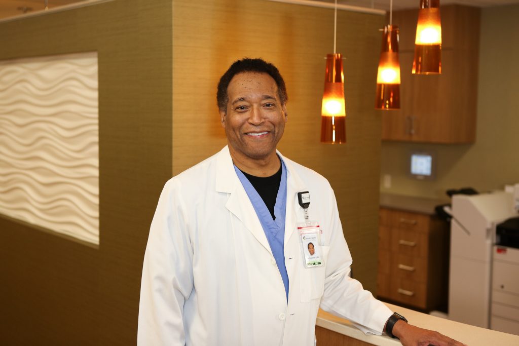 Dr. John W. Robertson III standing with his arm resting at the front desk of the nurses station