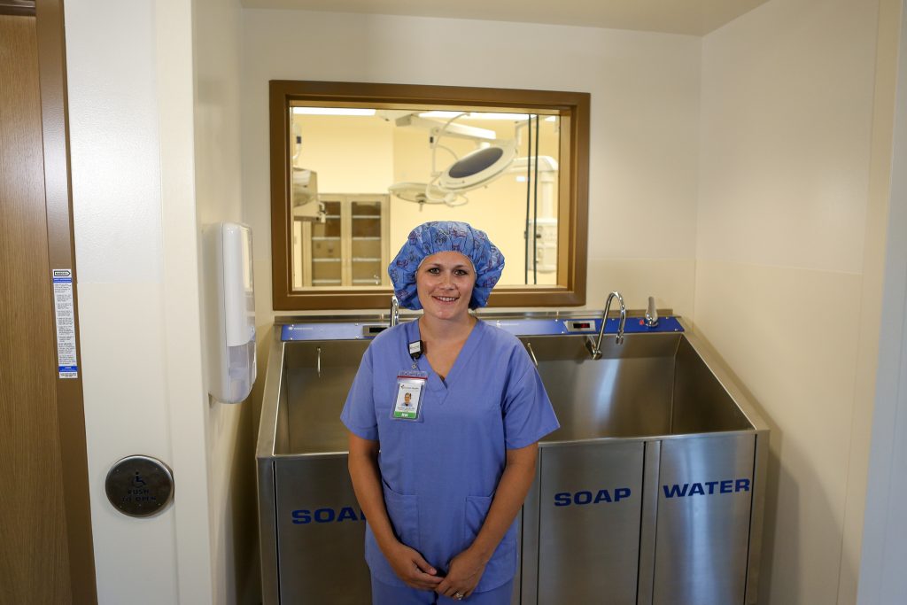 Jennifer Hutson in full scrubs and hair covering next to a surgical sink