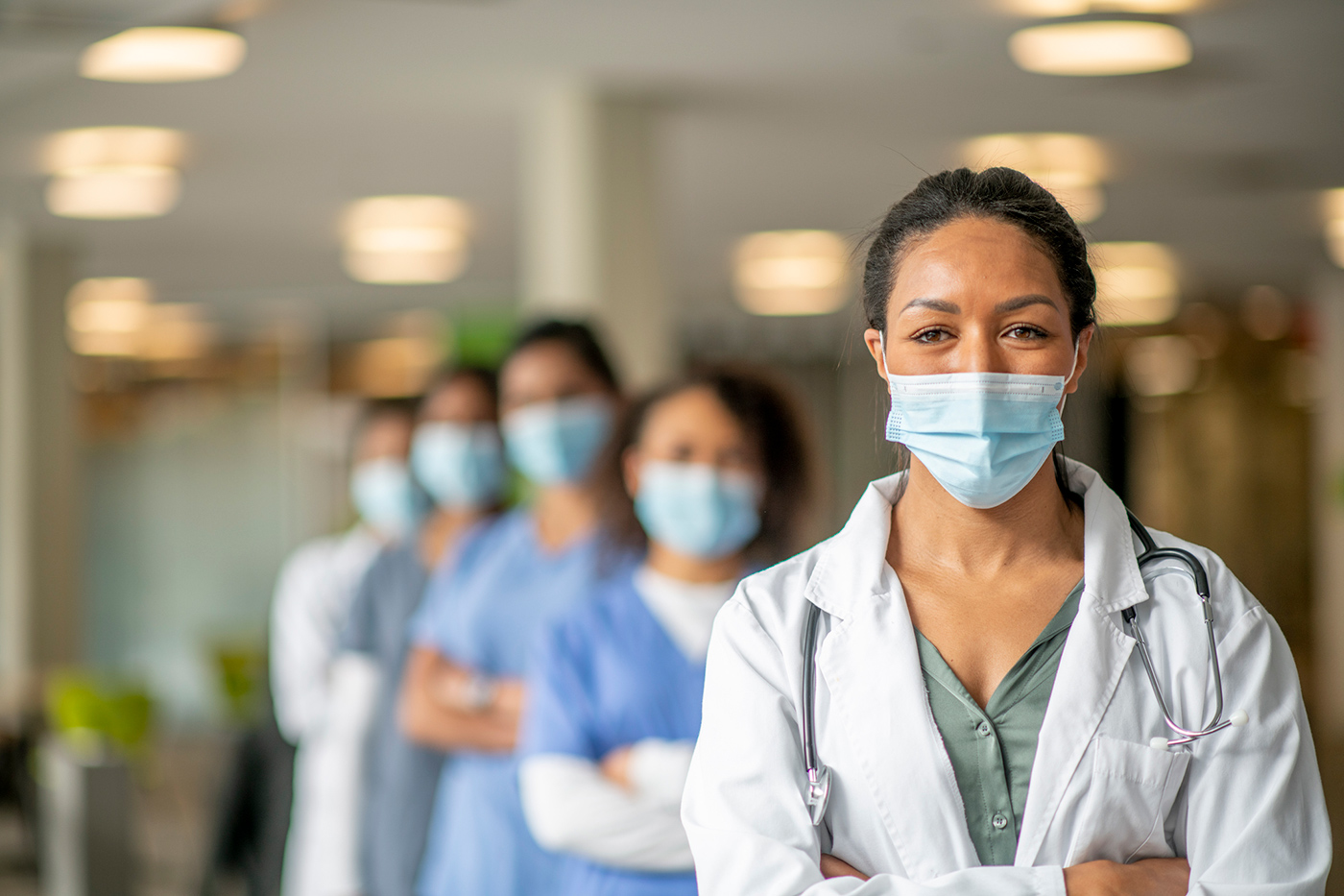 Doctors and nurses standing in a row with only the first female doctor in focus, all wearing surgical masks