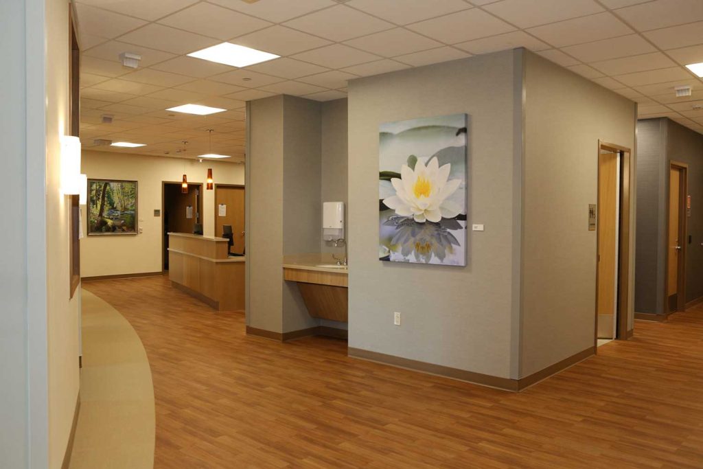 A hall in the interior of the hospital with art on the wall, doorways, and a water fountain