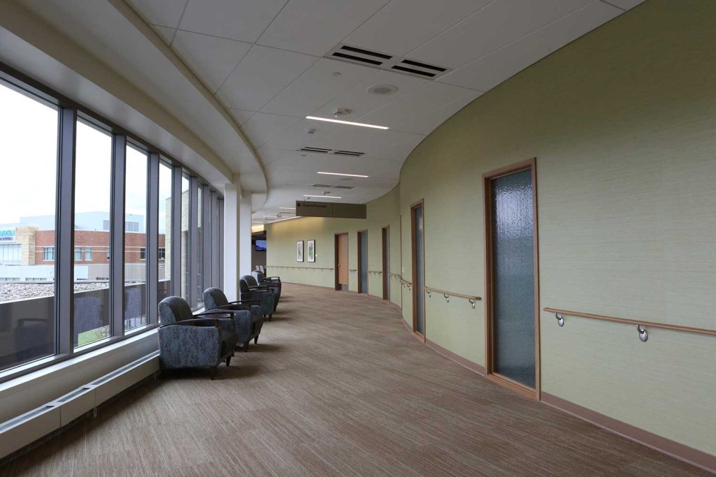 A hallway with comfortable looking chairs against windows on the left and doorways on the right