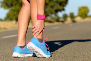 A runner grabbing her ankle in pain while standing on a bike path