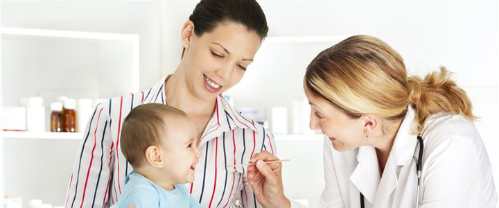 A mother sitting with a smiling baby on her lap while a female doctor give the baby a checkup