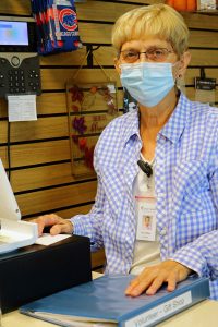 An older woman wearing a medical face mask, standing behind a giftshop cash register