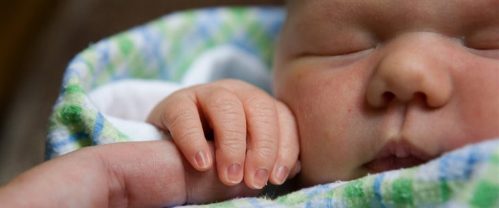 A very small baby sleeping while holding an adults finger in it's hand