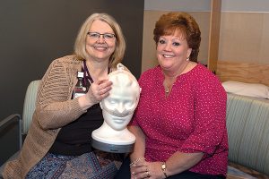 A nurse practitioner is showing a patient how to use a sleep apnea machine on a dummy's head