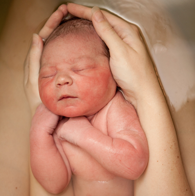 A woman holding a newborn on her bare legs in water