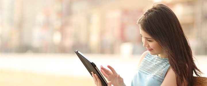 A woman sitting on a bench outdoors while looking at a tablet