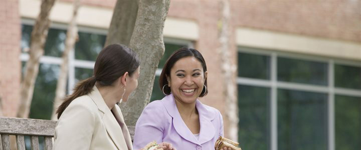 Two women sitting outside talking happily and eating sandwiches