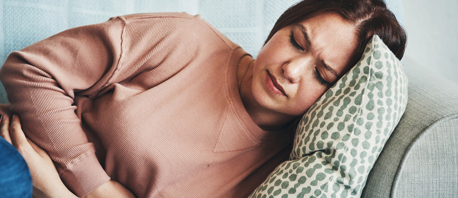 A woman lying on the couch holding her stomach in pain