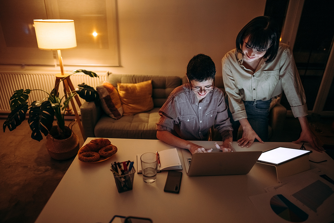 Two people looking at a laptop and tablet together at a table late at night