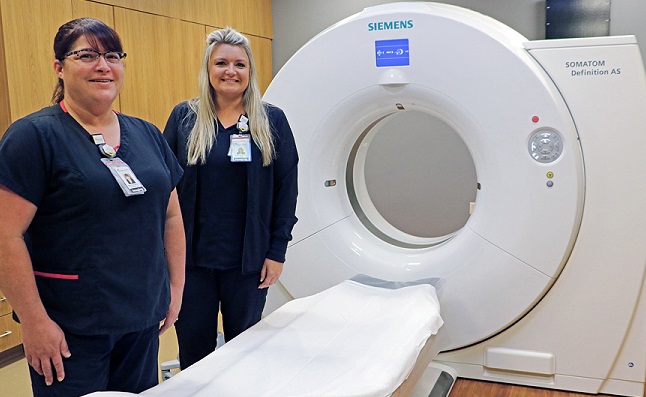 Two hospital staff members posing next to a large CT scanning machine