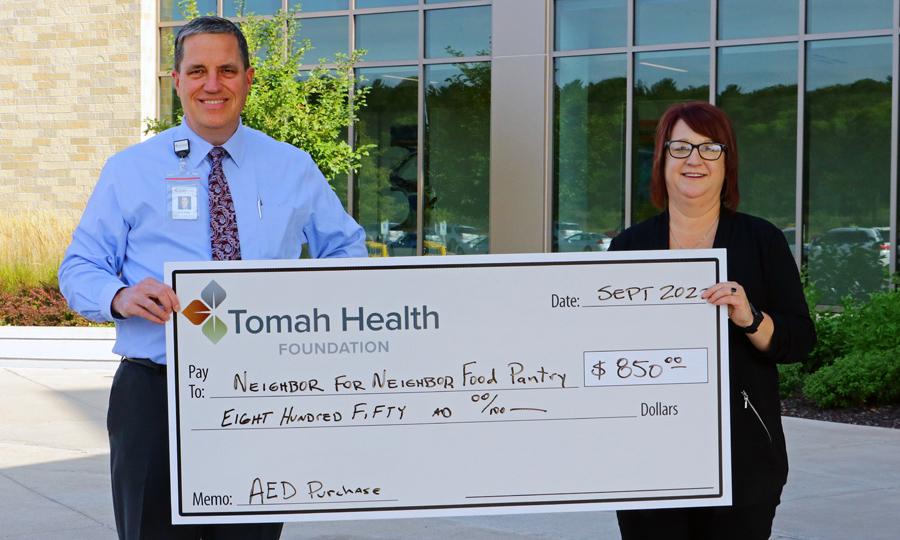 A TH staff member and a Neighbor for Neighbor Food Pantry staff member pose with a large check from Tomah Health Foundation