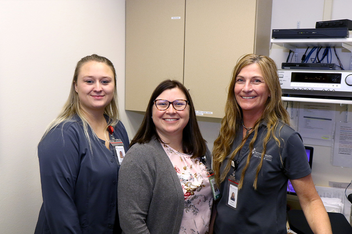 Three staff memebers at Tomah Health's Warrens Clinic posing together behind the front desk area